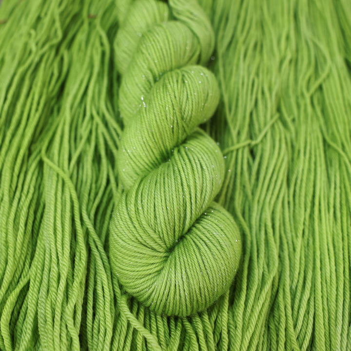 DK sparkle yarn colored a light bright green that is on top of an unwound skein of the same color.