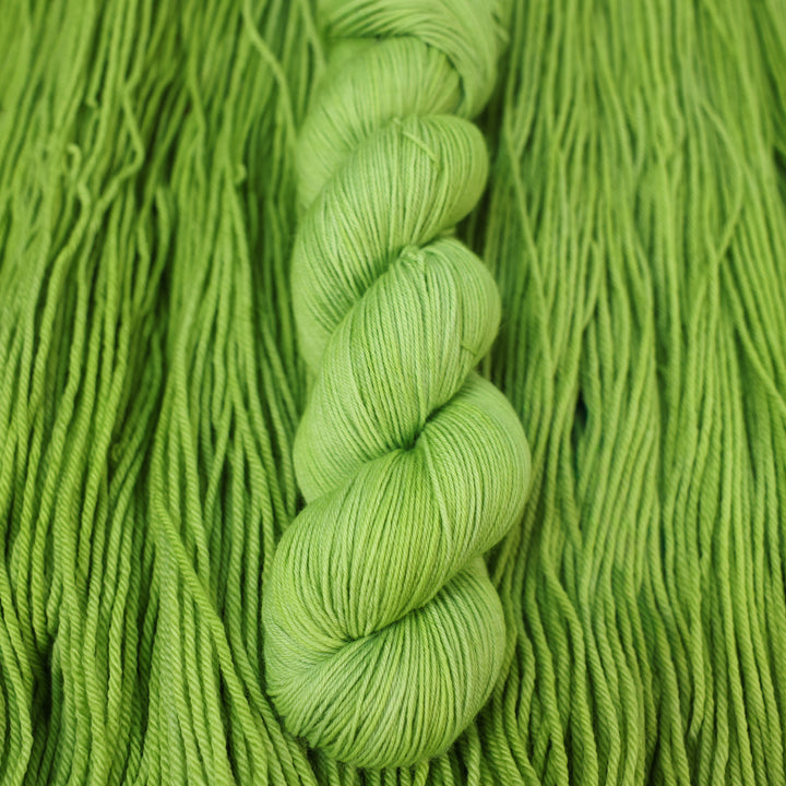 Fingering yarn colored a light bright green that is on top of an unwound skein of the same color.