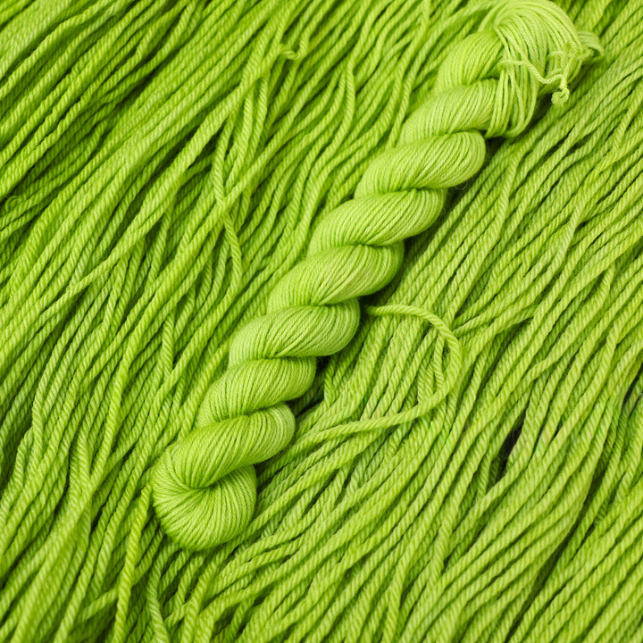 Fingering mini yarn colored a light bright green that is on top of an unwound skein of the same color.