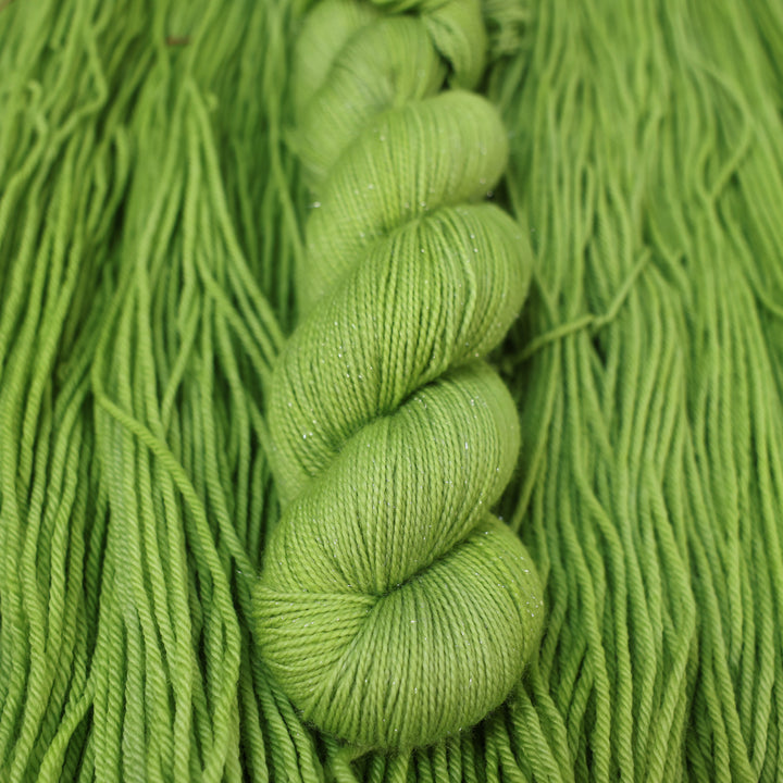 Fingering sparkle yarn colored a light bright green that is on top of an unwound skein of the same color.