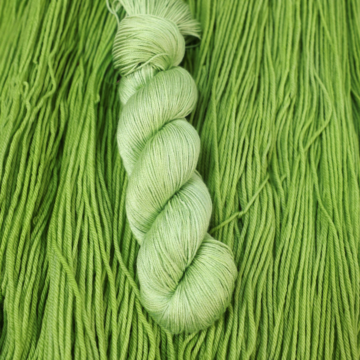 Silk yarn colored a light bright green that is on top of an unwound skein of the same color.