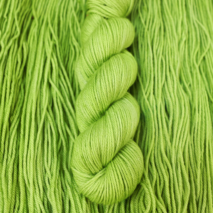 Worsted yarn colored a light bright green that is on top of an unwound skein of the same color.