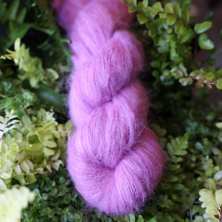 Suri alpaca yarn colored a light violet pink color. This skein is on top of a bed of ferns and plants