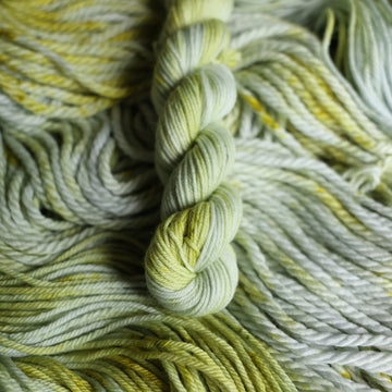 Mini yarn colored with different shades of light green and white with some dark green speckles on top of the same unwound yarn.