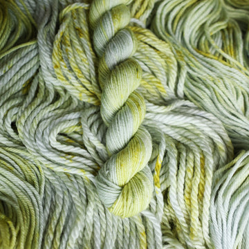 Mini-2 yarn colored with different shades of light green and white with some dark green speckles on top of the same unwound yarn.
