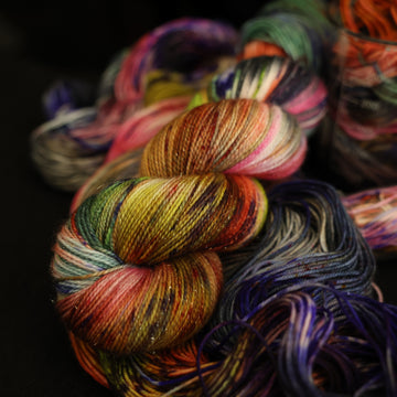 Multi colored sparkle yarn on top with more unwound multi colored yarn underneath and in a science beaker all on top of a black table