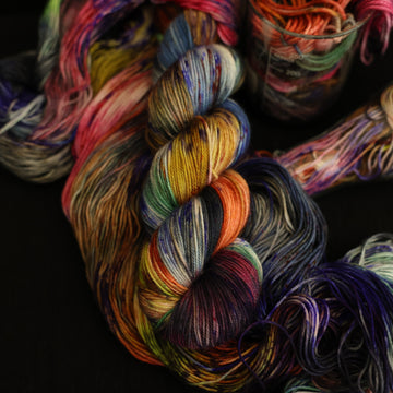 Multi colored sport yarn on top with more unwound multi colored yarn underneath and in a science beaker all on top of a black table