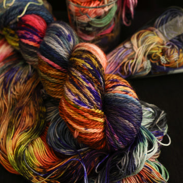 Multi colored bulky yarn on top with more unwound multi colored yarn underneath and in a science beaker all on top of a black table