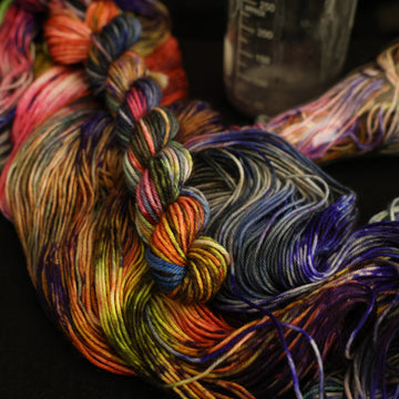 Multi colored mini yarn on top with more unwound multi colored yarn underneath and in a science beaker all on top of a black table