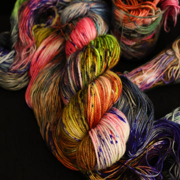 Multi colored worsted yarn on top with more unwound multi colored yarn underneath and in a science beaker all on top of a black table