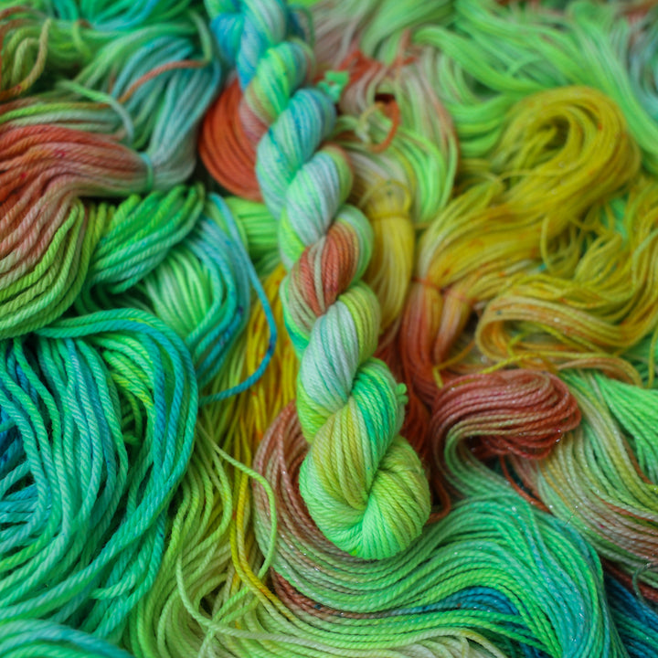DK mini yarn colored different colors like a light neon green, light blue, some streaks of white, some red, and some yellow. This skein is on top of unwound skeins of the same color way.