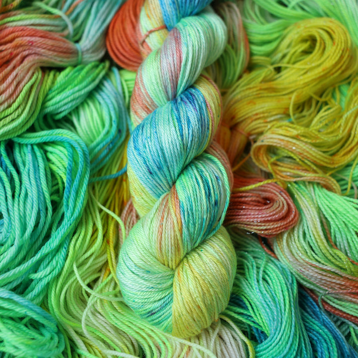 Silk DK yarn colored different colors like a light neon green, light blue, some streaks of white, some red, and some yellow. This skein is on top of unwound skeins of the same color way.