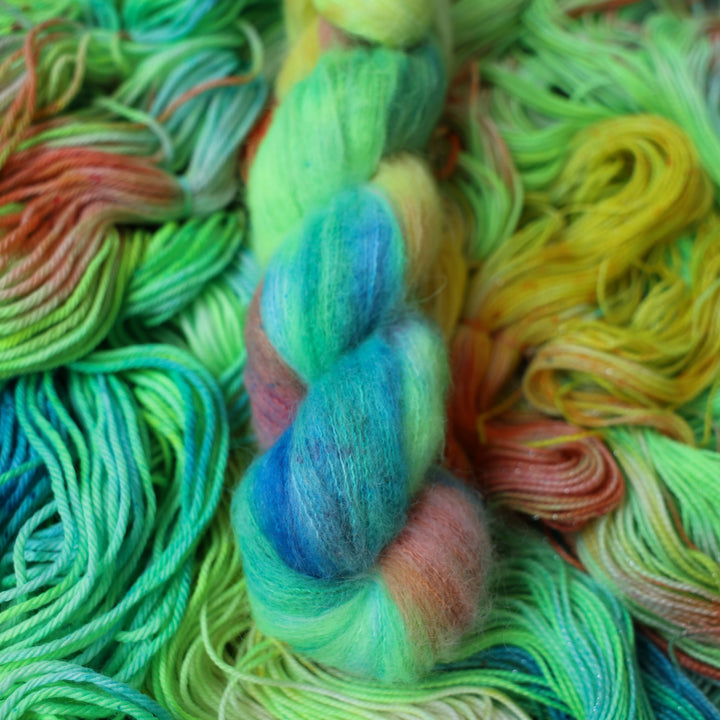 Suri yarn colored different colors like a light neon green, light blue, some streaks of white, some red, and some yellow. This skein is on top of unwound skeins of the same color way.