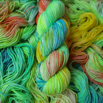 Worsted yarn colored different colors like a light neon green, light blue, some streaks of white, some red, and some yellow. This skein is on top of unwound skeins of the same color way.