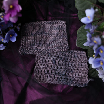 A crochet swatch colored  romantic plum-grey with moody grey and blue coloring. Surrounded by colorful flowers all sitting on top of a dark purple fabric.