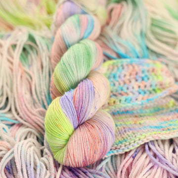 Multi colored light pastel colored fingering yarn with more unwound multi colored light pastel colored yarn underneath.