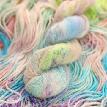 Multi colored light pastel colored suri yarn with more unwound multi colored light pastel colored yarn underneath.