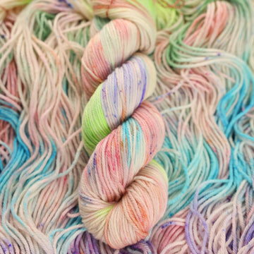 Multi colored light pastel colored worsted yarn with more unwound multi colored light pastel colored yarn underneath.