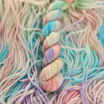 Multi colored light pastel colored mini-2 yarn with more unwound multi colored light pastel colored yarn underneath.