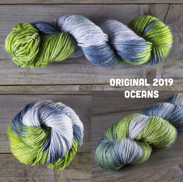 The green white and grey/blue yarn, two on top of a wooden table that is wound normally and one that is unwound but laid out in a spiral, also on a wooden table.