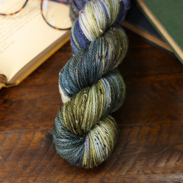 different colored blue green and white yarn on top of a wooden table with books in the top corners and a pair of glasses in the corner.