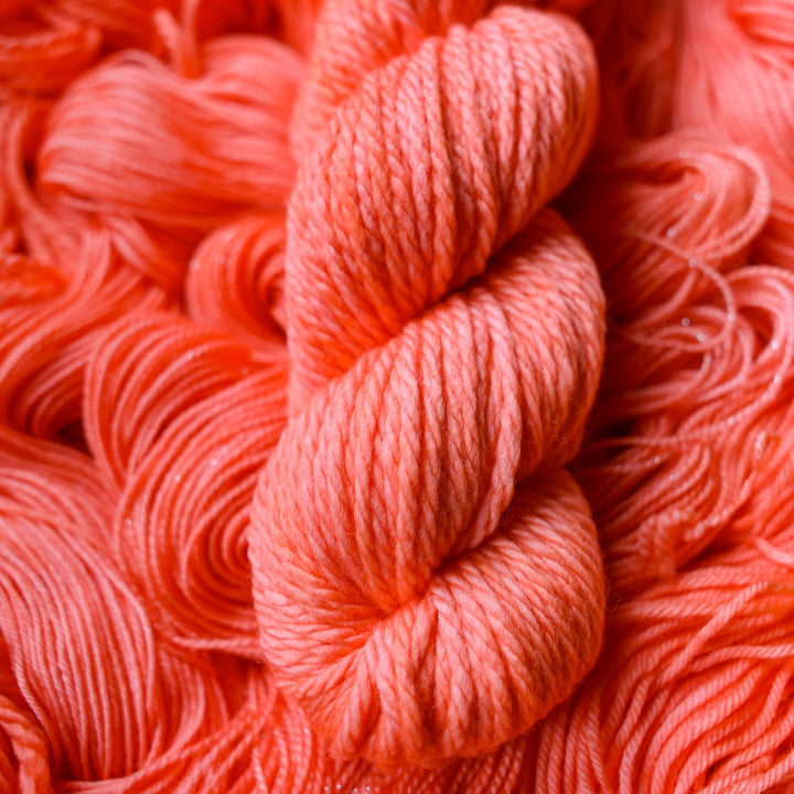 Bulky yarn colored a light pink color, this skein is on top of unwound skeins of this same color way.