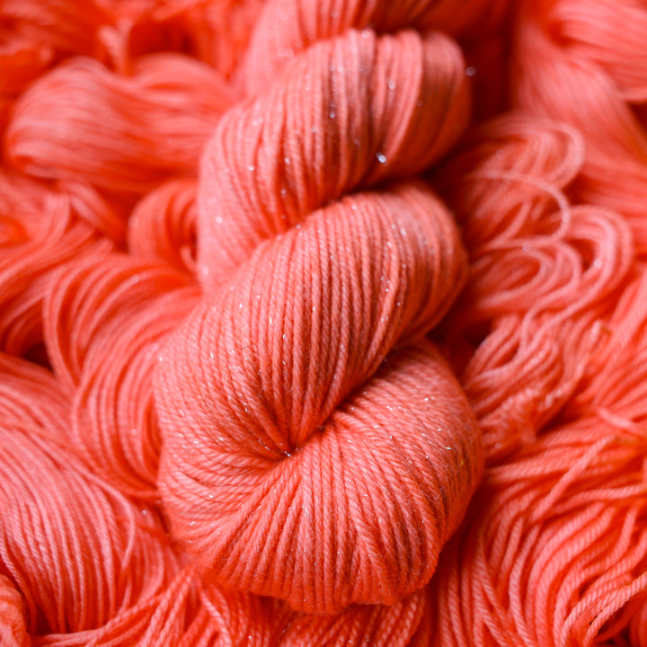 DK sparkle yarn colored a light pink color, this skein is on top of unwound skeins of this same color way.