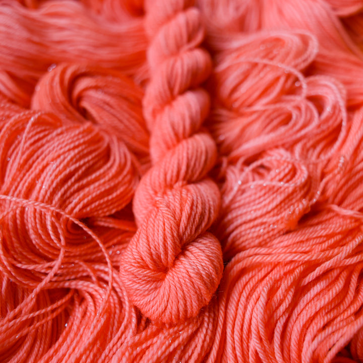 Fingering mini yarn colored a light pink color, this skein is on top of unwound skeins of this same color way.