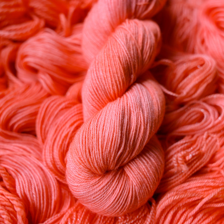 Fingering yarn colored a light pink color, this skein is on top of unwound skeins of this same color way.