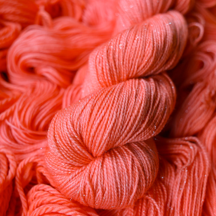 Fingering sparkle yarn colored a light pink color, this skein is on top of unwound skeins of this same color way.