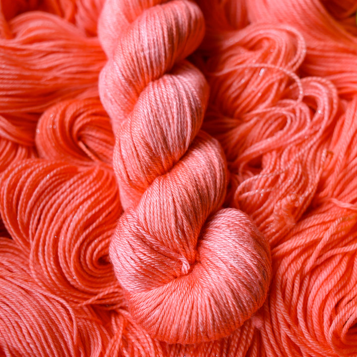 DK silk yarn colored a light pink color, this skein is on top of unwound skeins of this same color way.