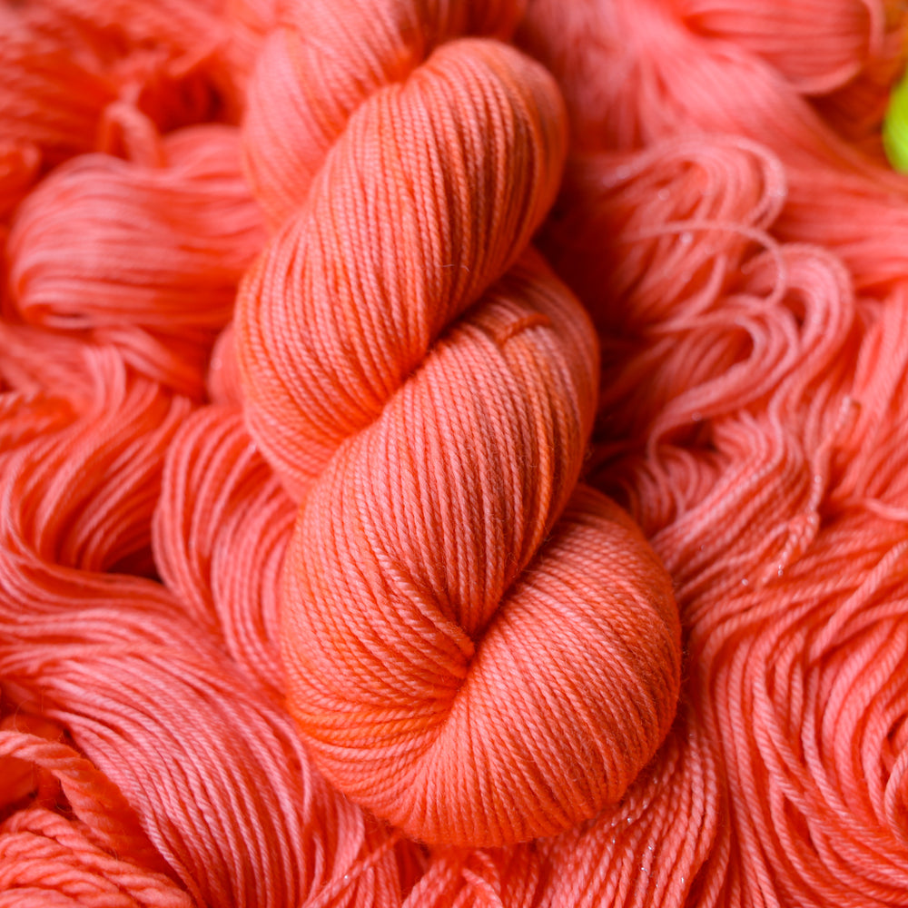 Sport yarn colored a light pink color, this skein is on top of unwound skeins of this same color way.