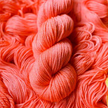 Worsted yarn colored a light pink color, this skein is on top of unwound skeins of this same color way.