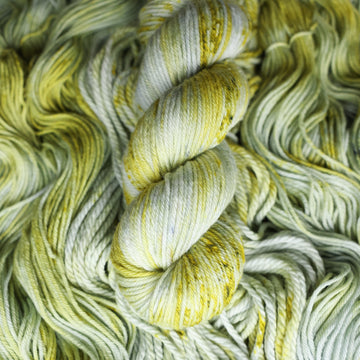 Worsted yarn colored with different shades of light green and white with some dark green speckles on top of the same unwound yarn.