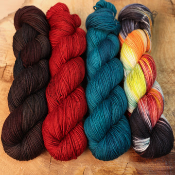 Prismflame yarn set on a wooden table, from left to right the colors are, brown and dark red with colored speckles, blue, and one skein that is brightly colored with red, orange, black, white and mint green.