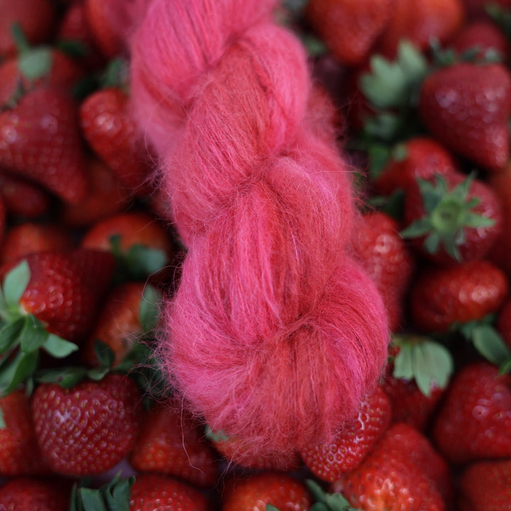 Suri yarn that is colored with different shades of pink like bright pink, and light pink, and a dark red and dark pink. This is on top of lots of ripe strawberries.