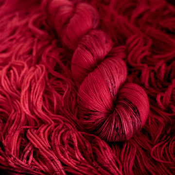 A vibrant red colored fingering yarn with some dark speckles, on top of an unwound version of that same yarn.