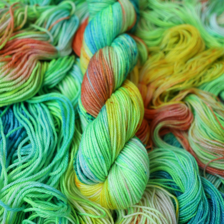 DK yarn colored different colors like a light neon green, light blue, some streaks of white, some red, and some yellow. This skein is on top of unwound skeins of the same color way.