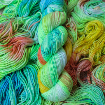 Sock yarn colored different colors like a light neon green, light blue, some streaks of white, some red, and some yellow. This skein is on top of unwound skeins of the same color way.