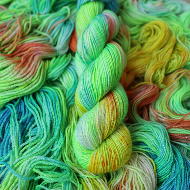 Sport yarn colored different colors like a light neon green, light blue, some streaks of white, some red, and some yellow. This skein is on top of unwound skeins of the same color way.