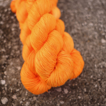 A couple of vibrant orange Silk yarn skeins on top of gravel.