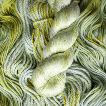 Silk yarn colored with different shades of light green and white with some dark green speckles on top of the same unwound yarn.