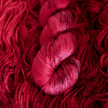 A vibrant red colored silk yarn with some dark speckles, on top of an unwound version of that same yarn.