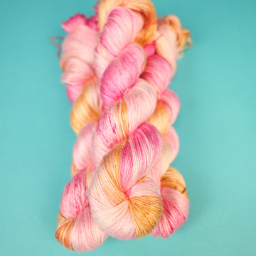 A couple of Silk yarn skeins that are colored with a light pink, yellow, and orang e, on top of a light blue background.