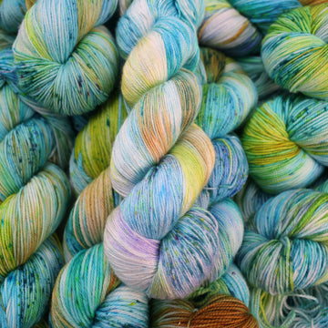 Silk yarn with light shades of blue and speckles of purple, with some light greens and browns. There are more skeins like this of different weights underneath.