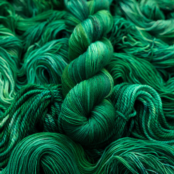 An emerald green colored S-mini yarn that is on top of the same colored unwound yarn in different weights.
