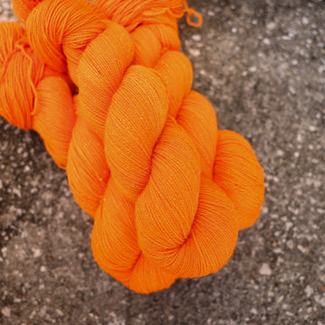A couple of vibrant orange Sparkle yarn skeins on top of gravel.