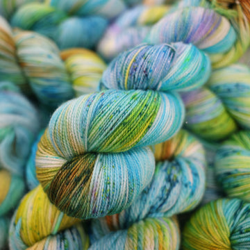 Sparkle yarn with light shades of blue and speckles of purple, with some light greens and browns. There are more skeins like this of different weights underneath.