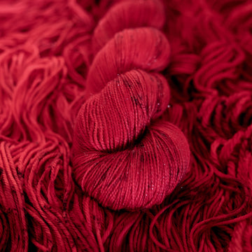 A vibrant red colored Sparkle yarn with some dark speckles, on top of an unwound version of that same yarn.