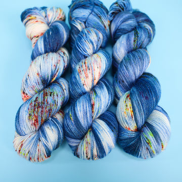 Sparkle yarn colored with different shades of blue and white with multicolored speckles on the portion of the yarn that Is white. all on top of a light blue background.